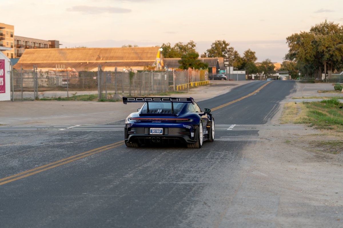 Rear view of a blue 2025 Porsche 911 GT3 RS with a large rear wing, white rims, and quad exhaust pipes.