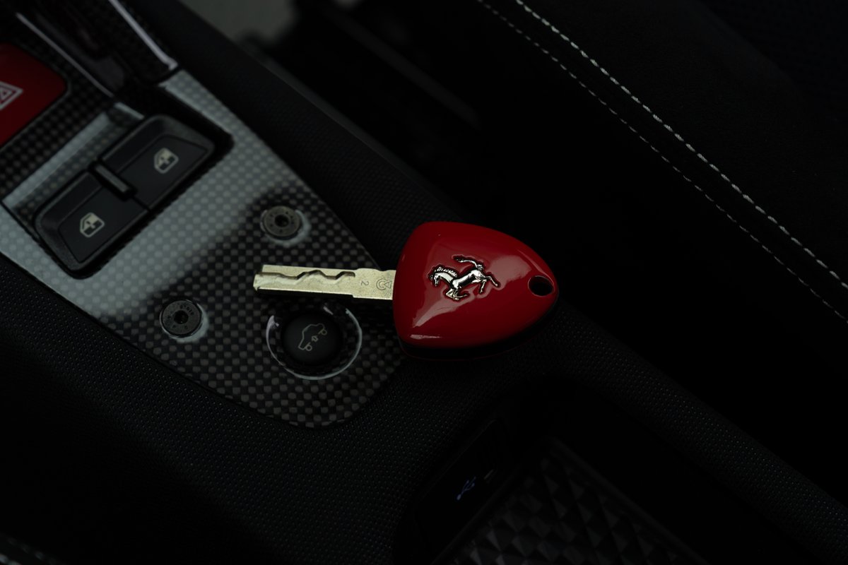 Red Ferrari 458 Speciale key on carbon fiber trim with prancing horse emblem.