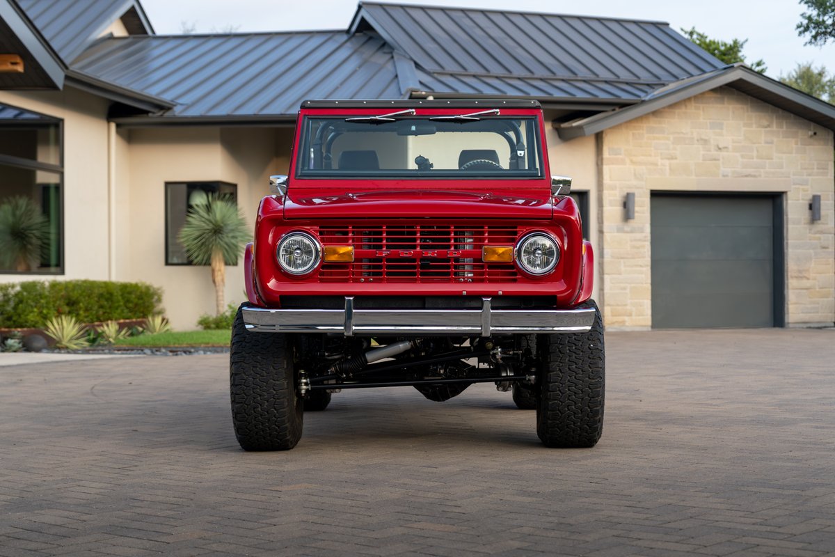 Front view of a red 1966 Ford Bronco with chrome trim and large off-road rims.