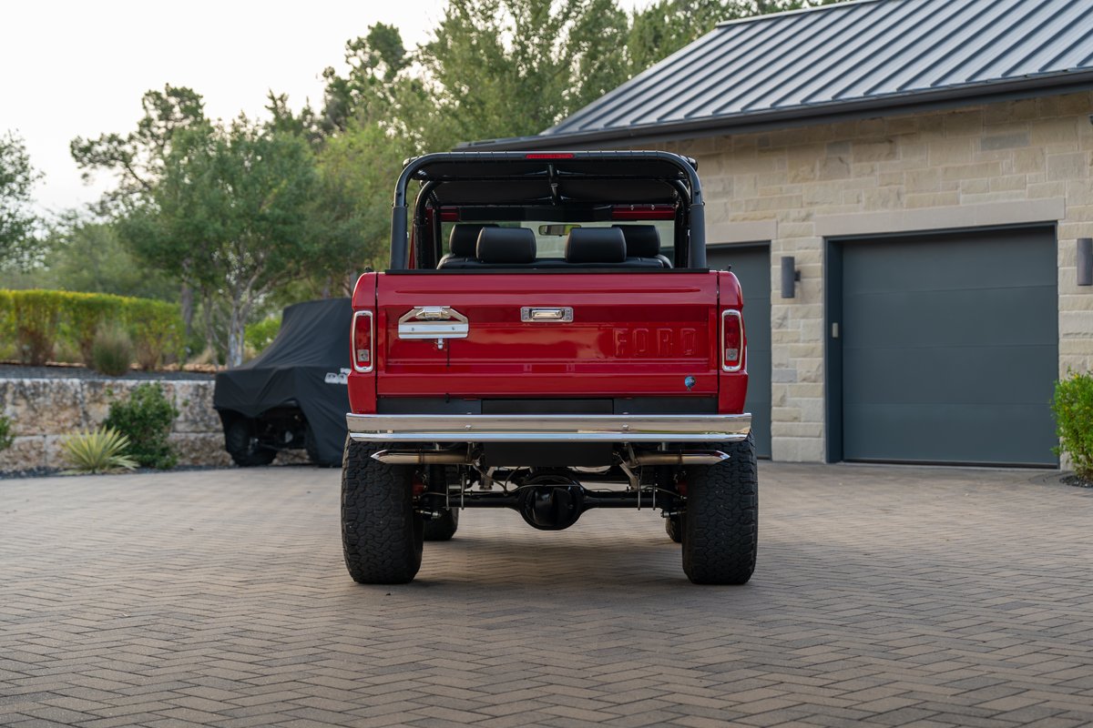 Red 1966 Ford Bronco with aftermarket exhaust and large off-road tires.