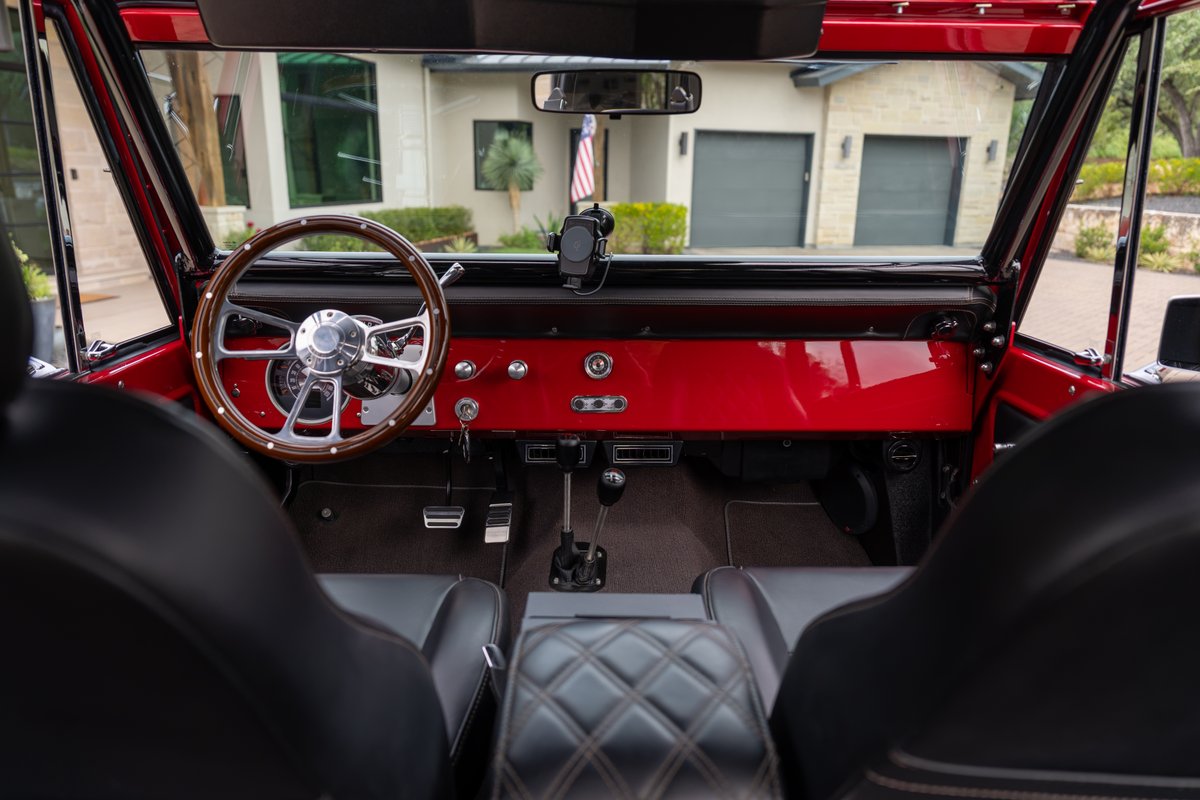 1966 Ford Bronco interior in red, featuring a wood-rimmed steering wheel and black leather seats.
