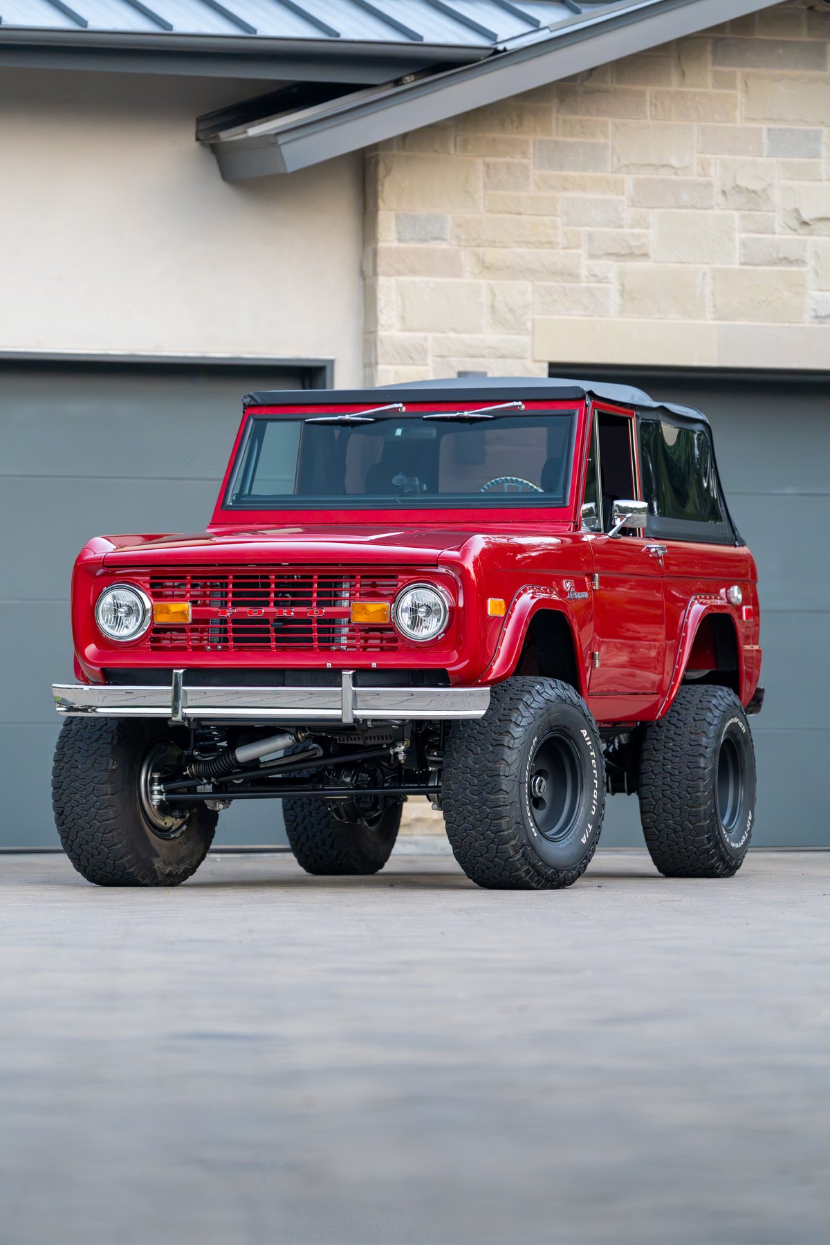 Red 1966 Ford Bronco with black soft top, chrome bumper, and all-terrain tires on black rims.
