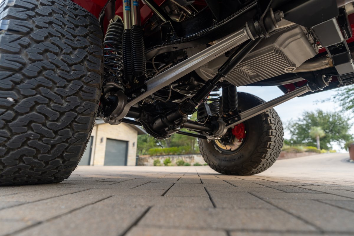 Close-up of a red 1966 Ford Bronco's custom suspension, off-road tires, and ZPE oil pan.