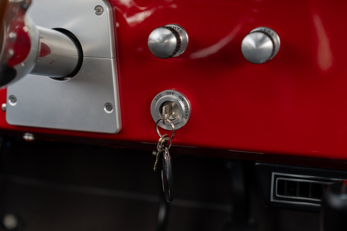 Close-up of a 1966 Ford Bronco dashboard in red with silver trim, ignition and light switches.