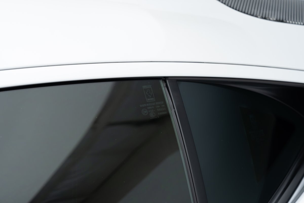 Close-up of a white 2015 Ferrari 458 Speciale window with manufacturer's markings.