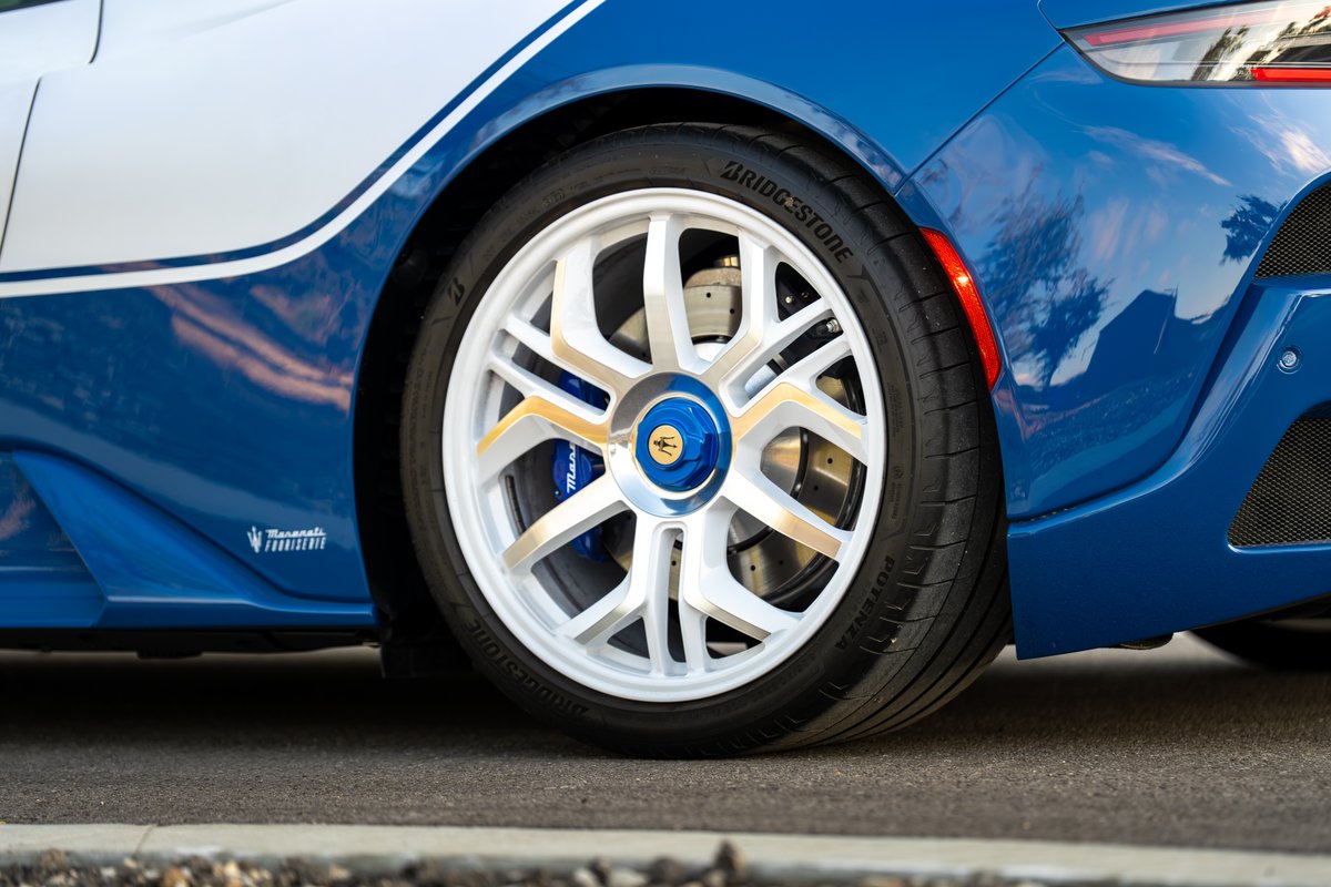 Maserati MC20 Icona in blue with white and gold livery, white rims, Bridgestone tires.