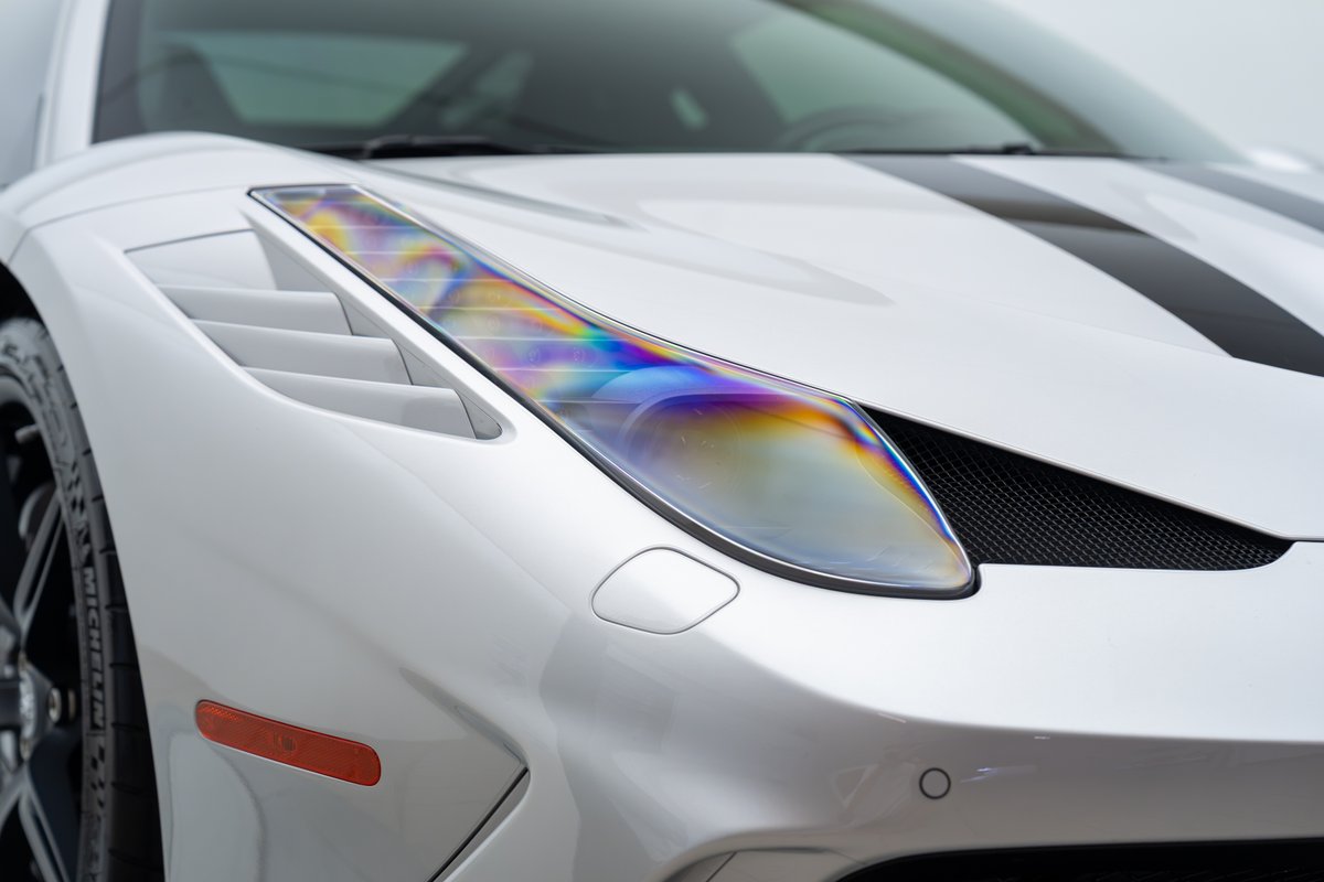 White 2015 Ferrari 458 Speciale with black racing stripes and iridescent headlights.