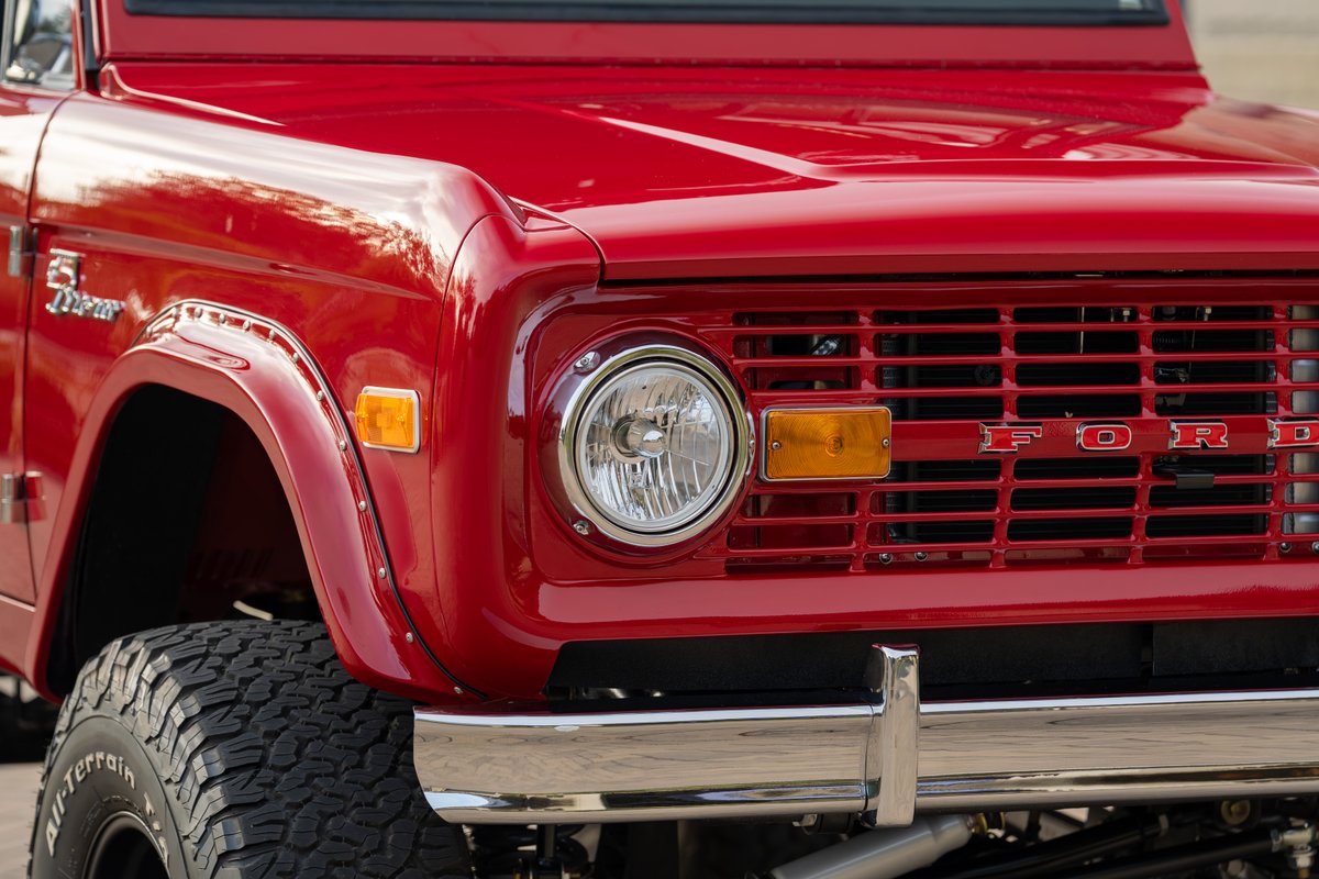 Front view of a red 1966 Ford Bronco, showing its chrome bumper, grille, and headlight.