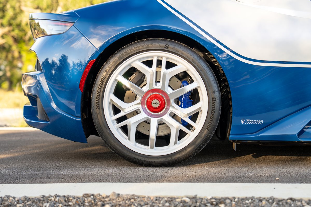 2024 Maserati MC20 Icona rear wheel with silver rims, red center cap, and blue calipers.