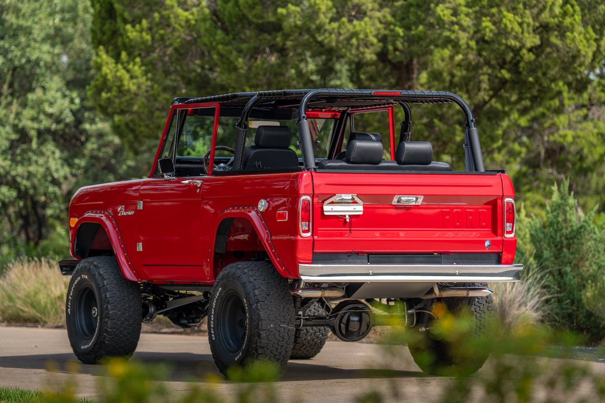 Rear view of a red 1966 Ford Bronco with off-road tires and a roll cage.