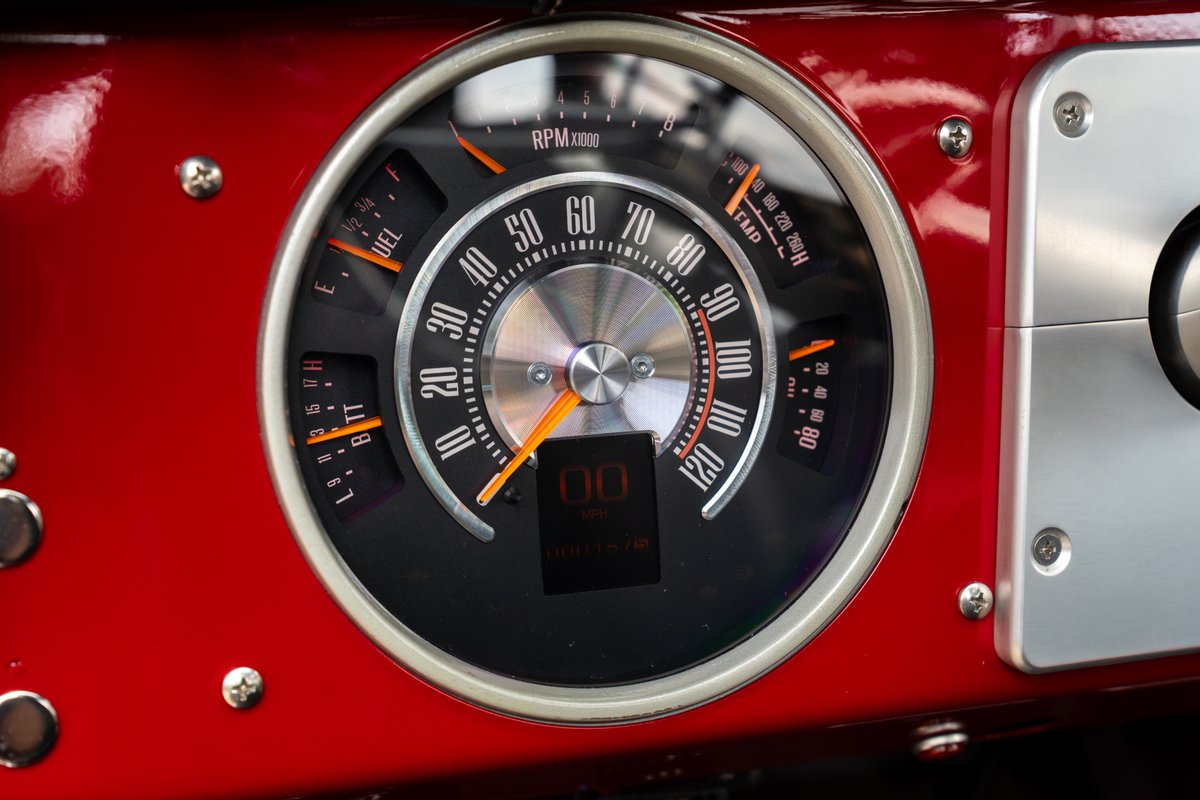 Close-up of a red 1966 Ford Bronco's custom instrument cluster with speedometer, tachometer, fuel and temp gauges.