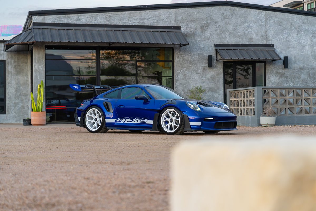 Blue 2025 Porsche 911 GT3 RS with white racing stripes and white rims parked outside.