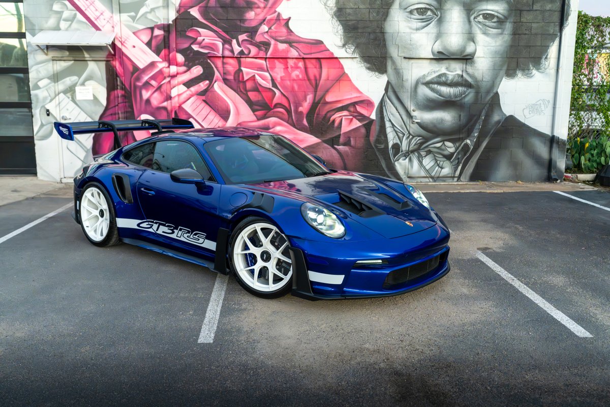 Blue 2025 Porsche 911 GT3 RS with white stripe livery and white racing rims.