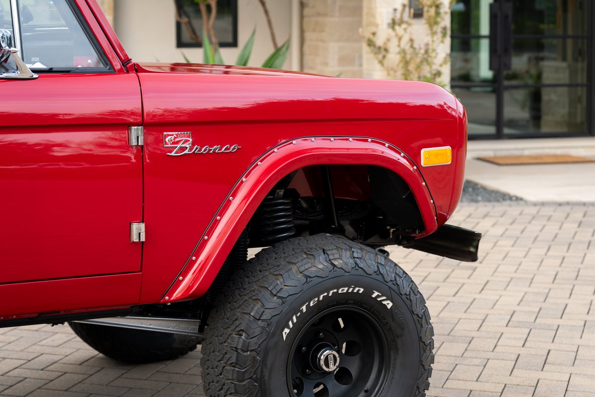 Red 1966 Ford Bronco fender, door, and BFGoodrich All-Terrain T/A tires on black rims.