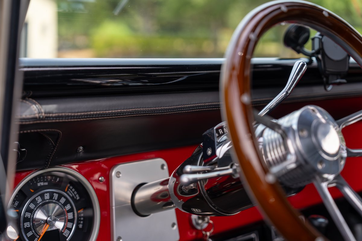 Classic 1966 Ford Bronco interior with wood steering wheel, chrome details, and red dash trim.