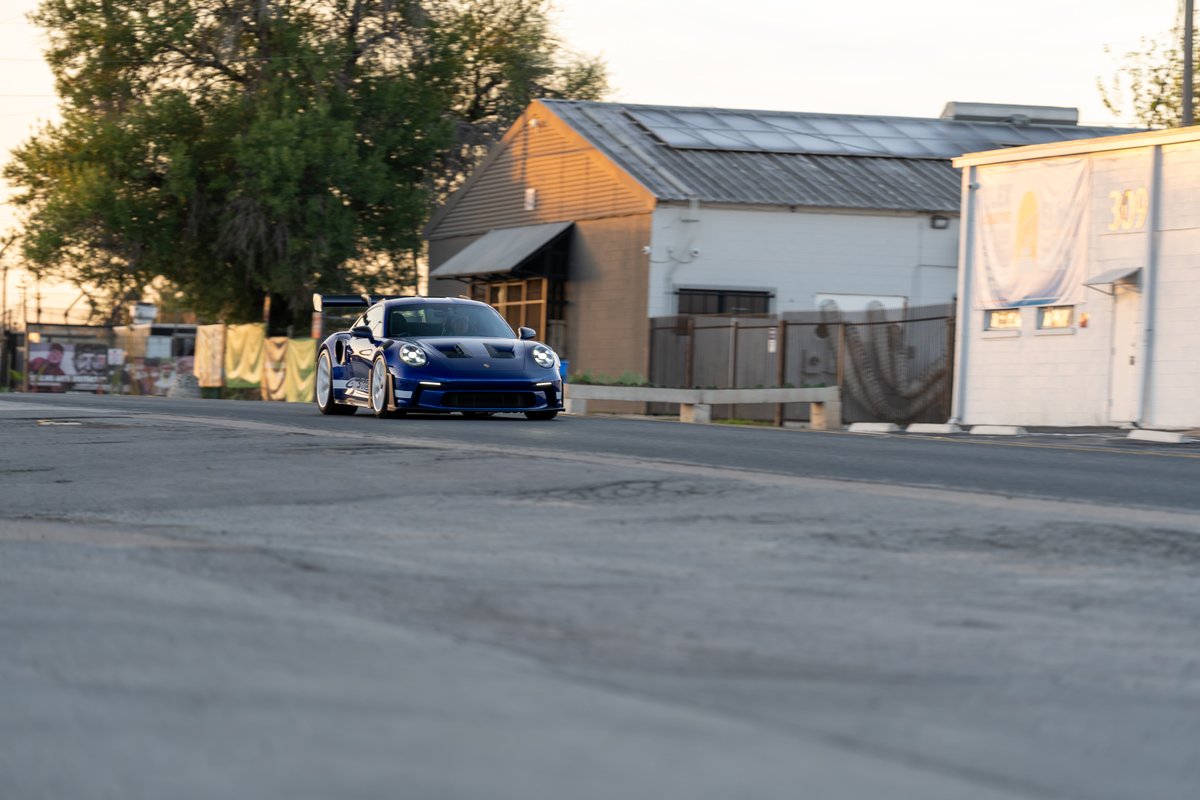 A blue 2025 Porsche 911 GT3 RS with silver rims and black brake calipers drives on asphalt.