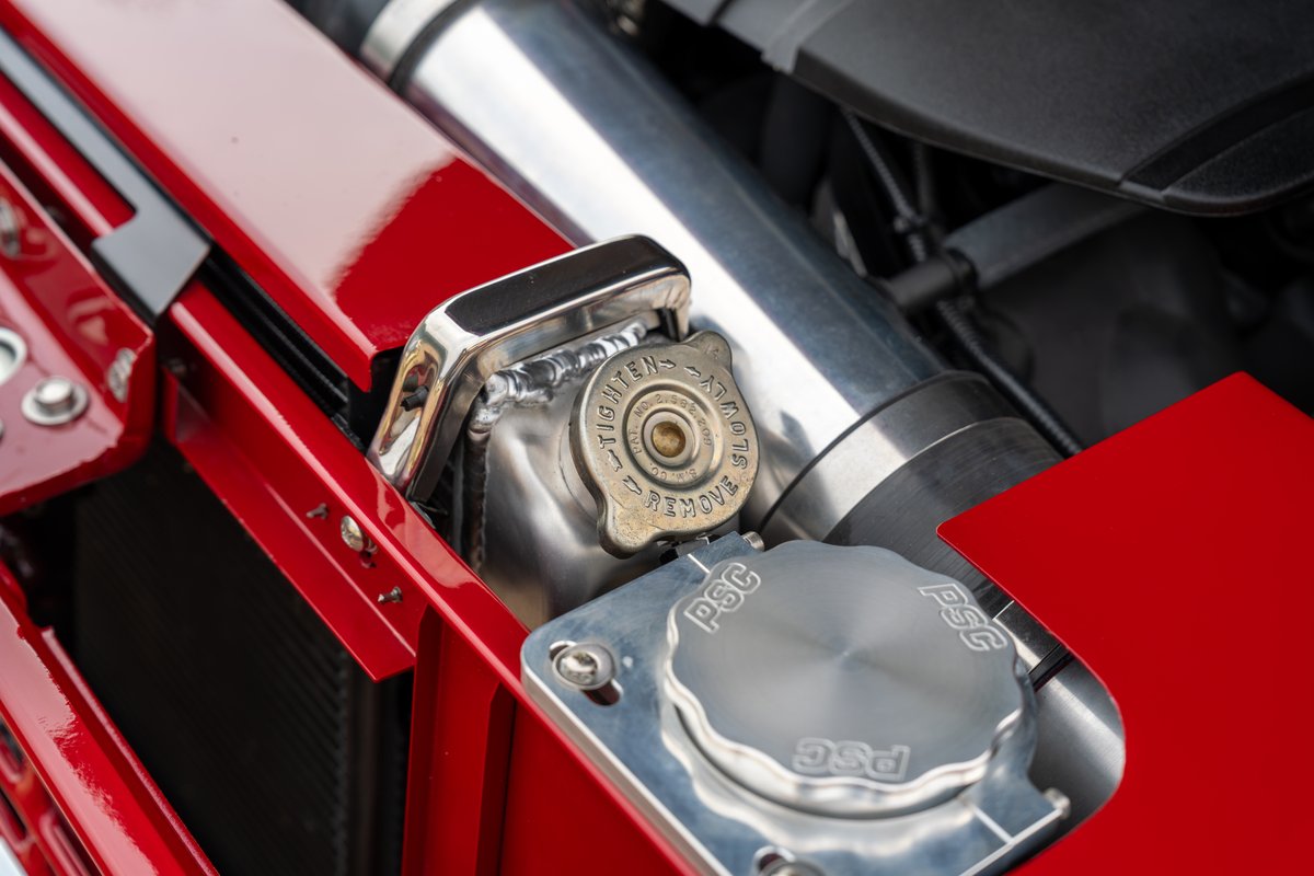 Close-up of a red 1966 Ford Bronco's engine bay, showing a polished aluminum radiator and caps.