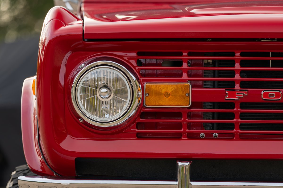 Close-up of a red 1966 Ford Bronco grille with a chrome headlight and amber turn signal.