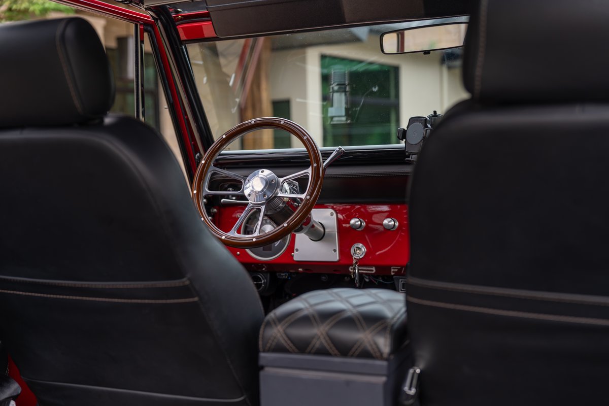 1966 Ford Bronco interior: classic wood-rimmed steering wheel, red dash trim, diamond-stitched center console.