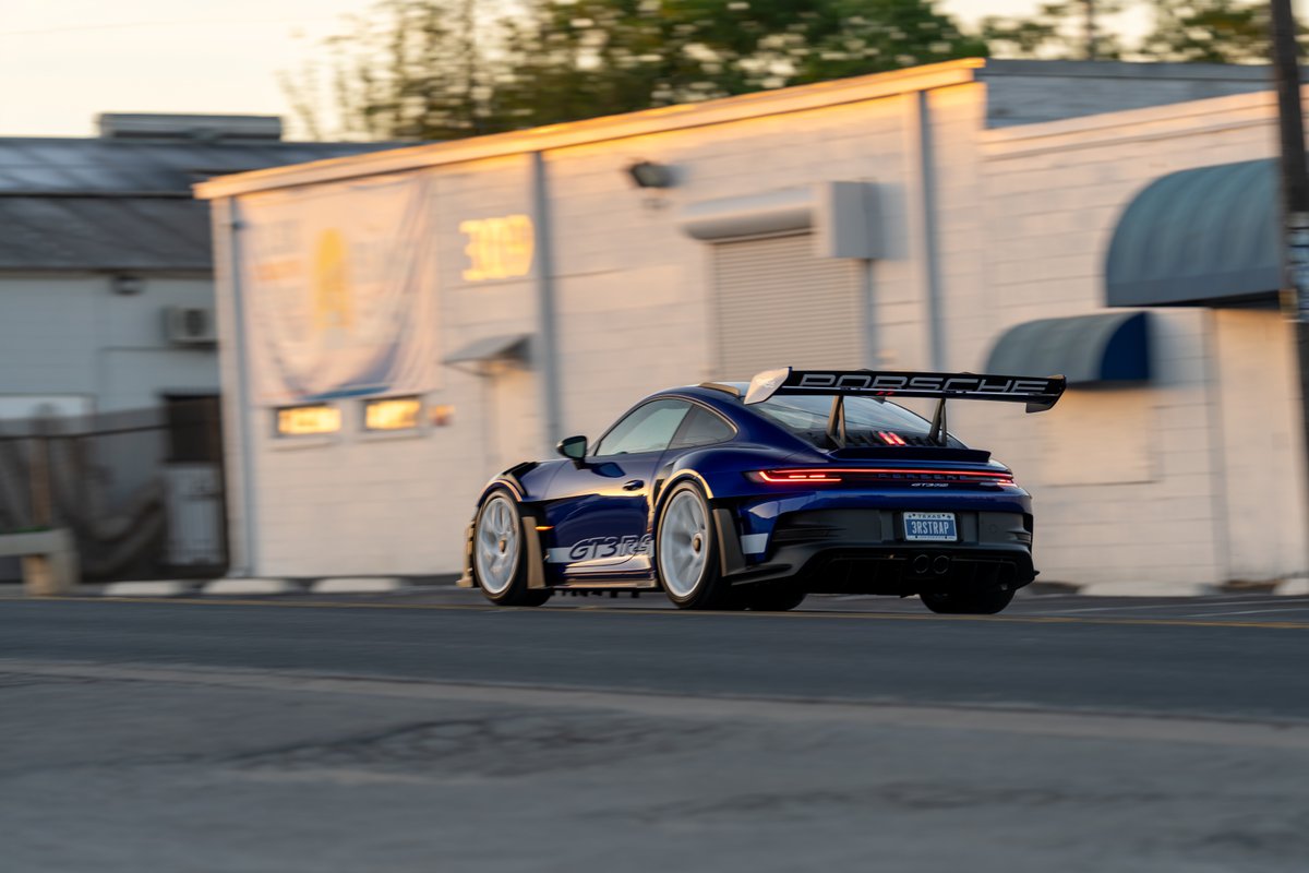 Rear view of a blue 2025 Porsche 911 GT3 RS with white rims and a large rear wing.