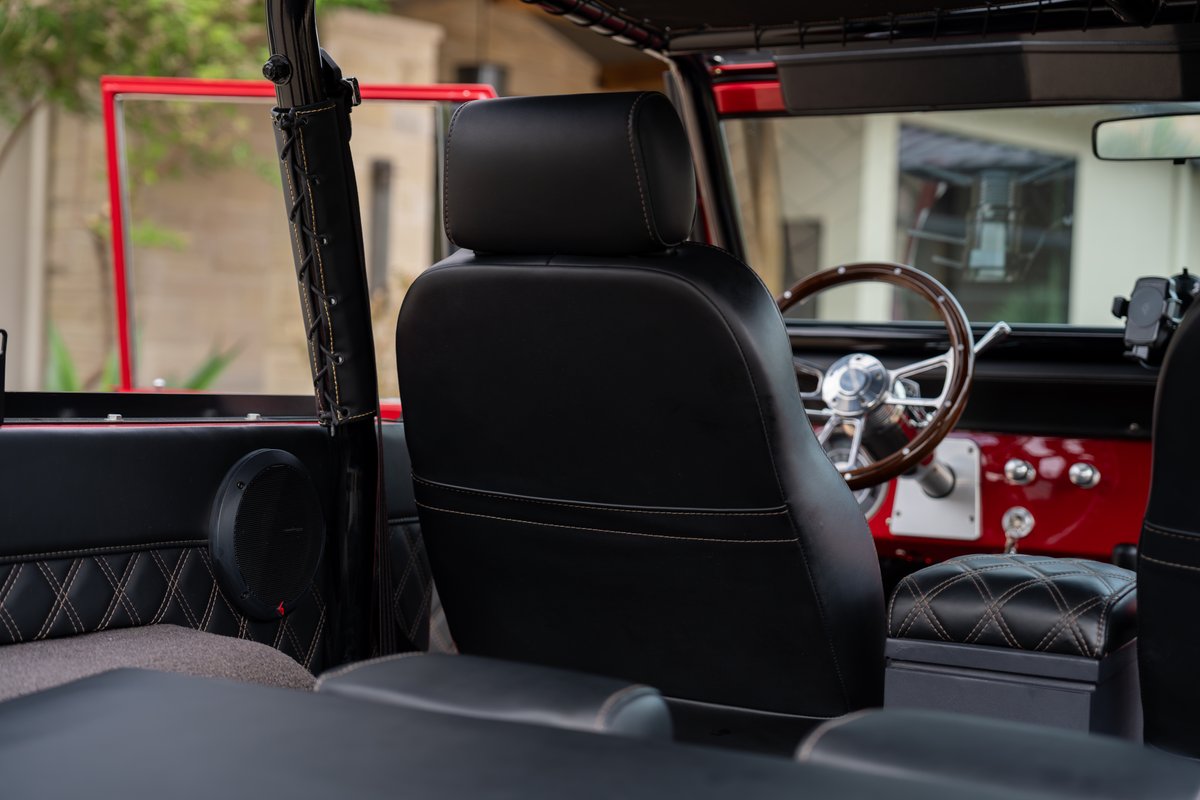 1966 Ford Bronco interior, black leather seats, diamond-stitched trim, wood steering wheel.