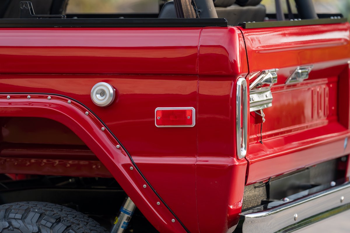 Close-up of a red 1966 Ford Bronco's rear quarter panel, featuring a fuel cap and chrome trim.