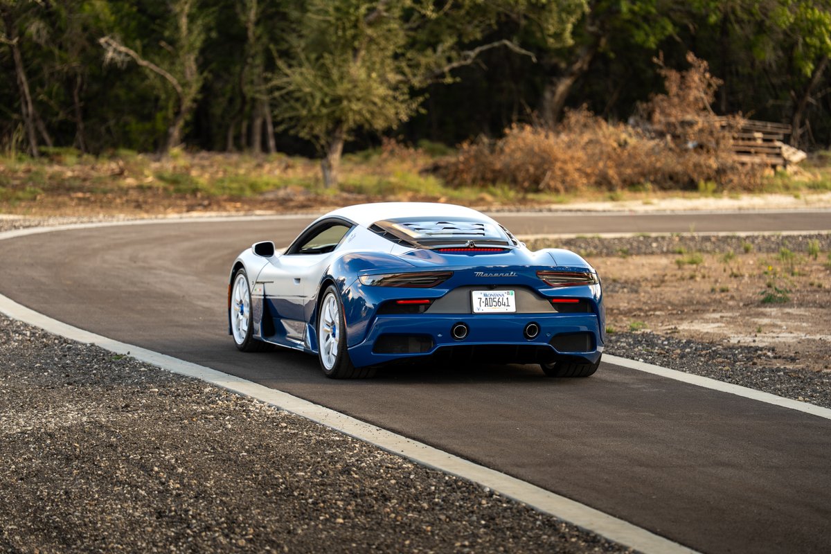Rear view of a blue and white 2024 Maserati MC20 Icona with white rims on a paved road.