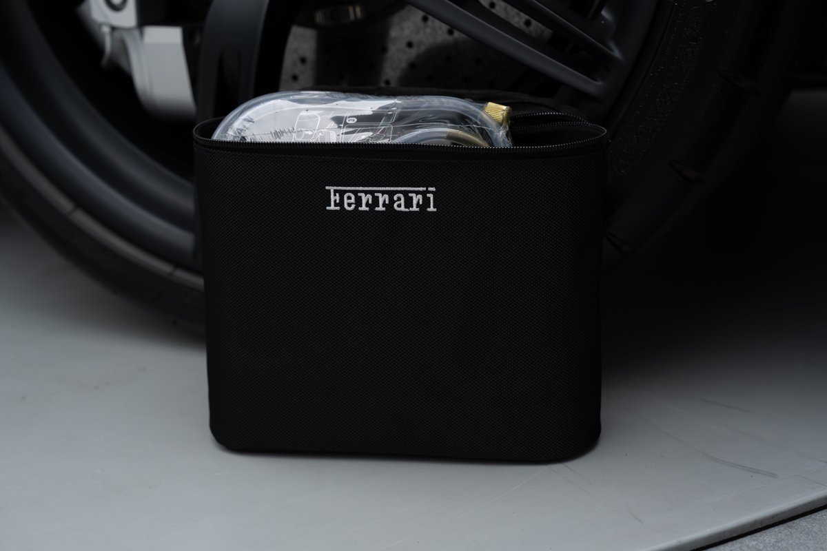 Black Ferrari storage bag with headlight kit, next to a 458 Speciale wheel and tire.