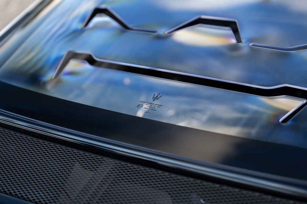 Maserati MC20 Icona: Closeup of blue tinted windshield with black trim & Maserati logo.