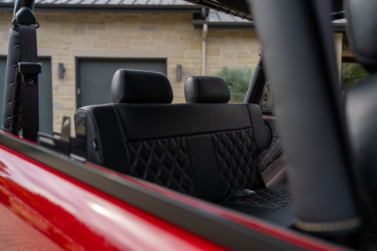 1966 Ford Bronco interior with black diamond-stitched seats, red exterior trim, and roll cage.