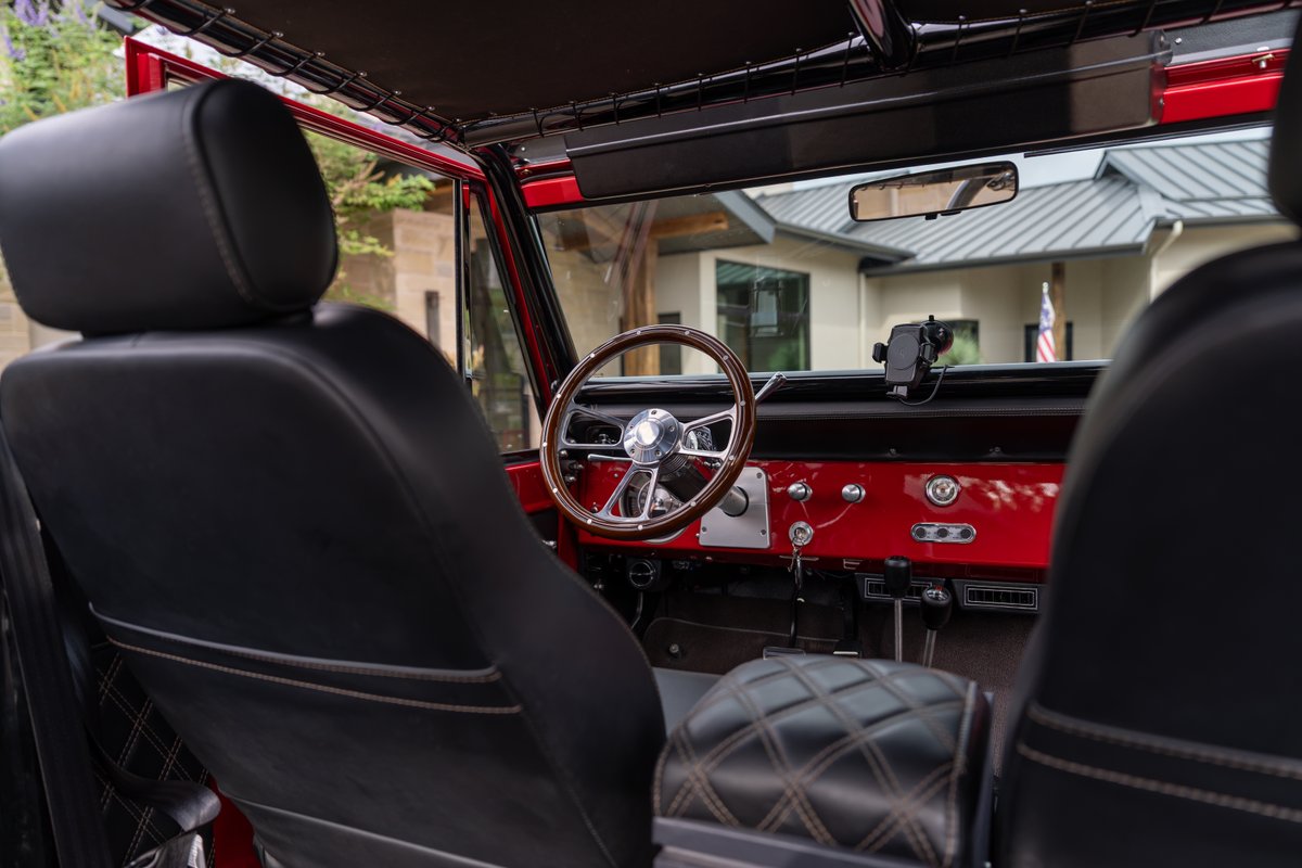 1966 Ford Bronco interior in red, with black diamond-stitched seats and a wood-rimmed steering wheel.