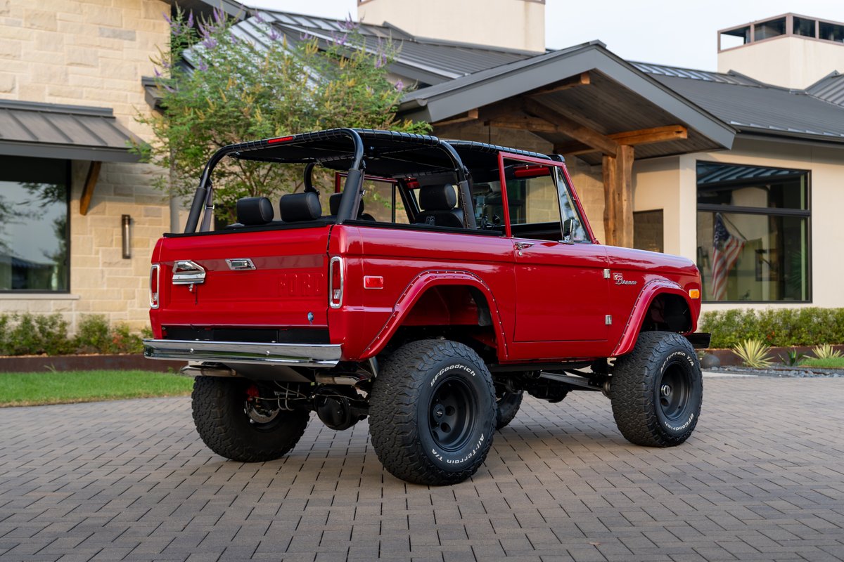 Red 1966 Ford Bronco by Atlas Broncos with black rims and off-road tires.