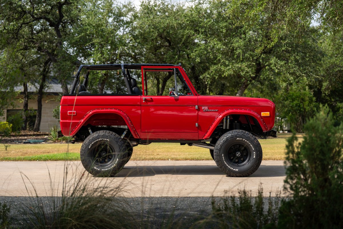 1966 Ford Bronco in red with black roll cage and BFGoodrich all-terrain tires on black rims.