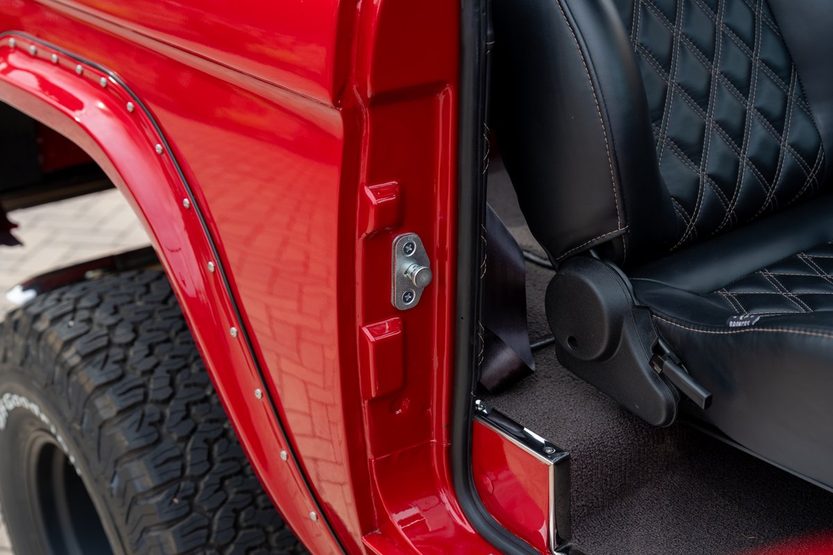 Red 1966 Ford Bronco features a diamond-stitched black leather seat and rugged off-road tires.
