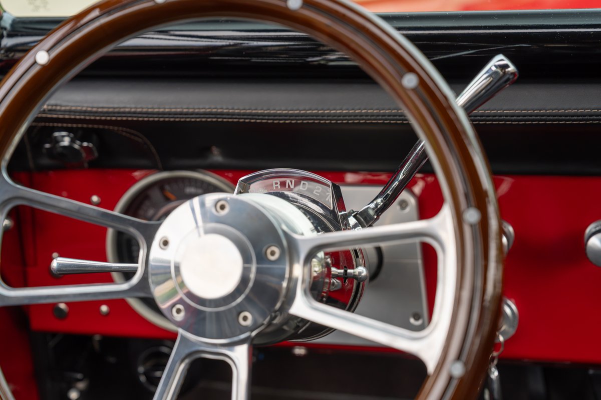 Close-up of a vintage 1966 Ford Bronco's wood-rimmed steering wheel and chrome shifter.