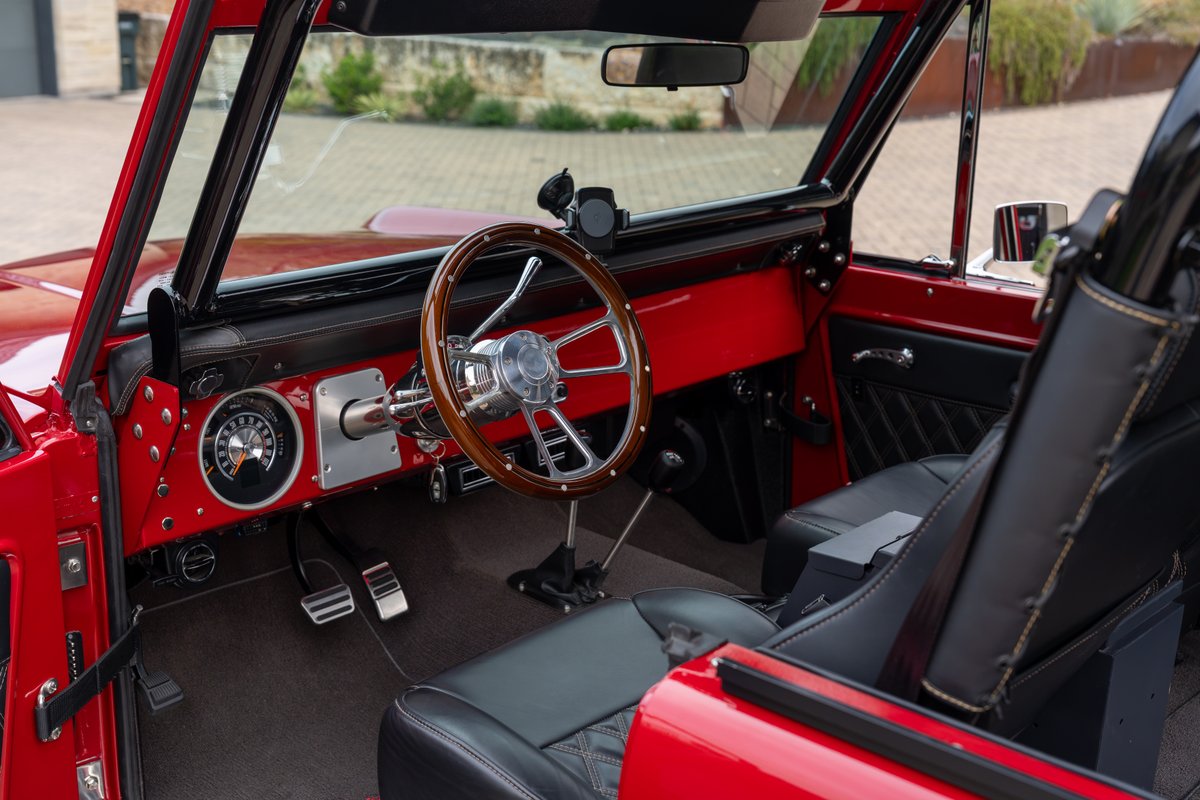 Red 1966 Ford Bronco interior featuring a wood-rimmed steering wheel and diamond-stitched black leather seats.