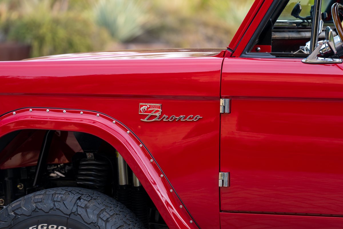 Red 1966 Ford Bronco fender with chrome Bronco emblem and rivet trim.