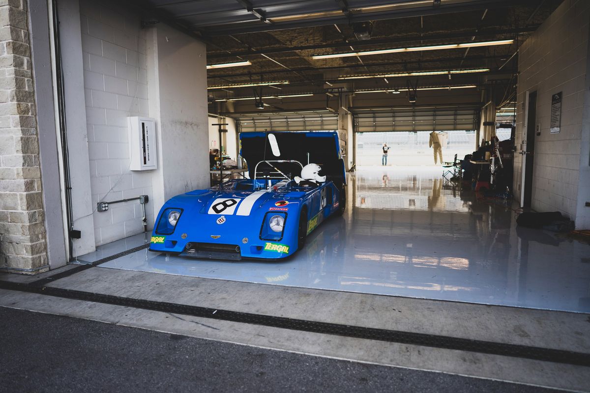 Blue Lola T70 Mk.IIIb vintage Can-Am prototype racer, #8 livery, black rims, in COTA pit garage.