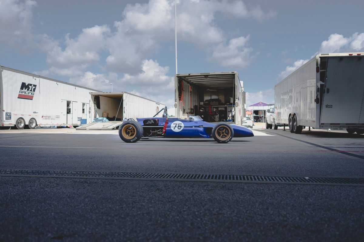 Vintage open-wheel race car #75, blue livery, gold multi-spoke rims, Avon slicks, COTA Classic Race Series paddock.