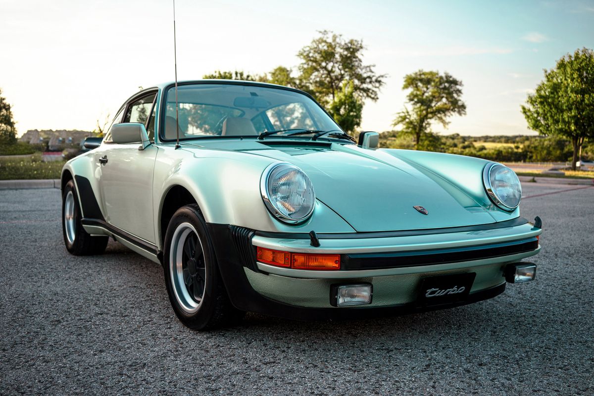 Front view of a 1976 Porsche 930 Turbo in Ice Metallic Green, featuring its iconic wide body, Fuchs rims, and black bumper trim.