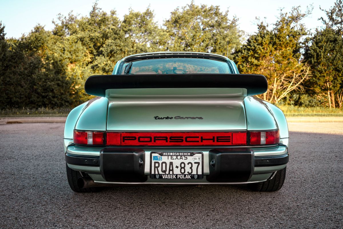 1976 Ice Metallic Green Porsche 930 Turbo rear, iconic whale tail wing, PORSCHE taillight bar, 'turbo Carrera' script, black bumperettes.