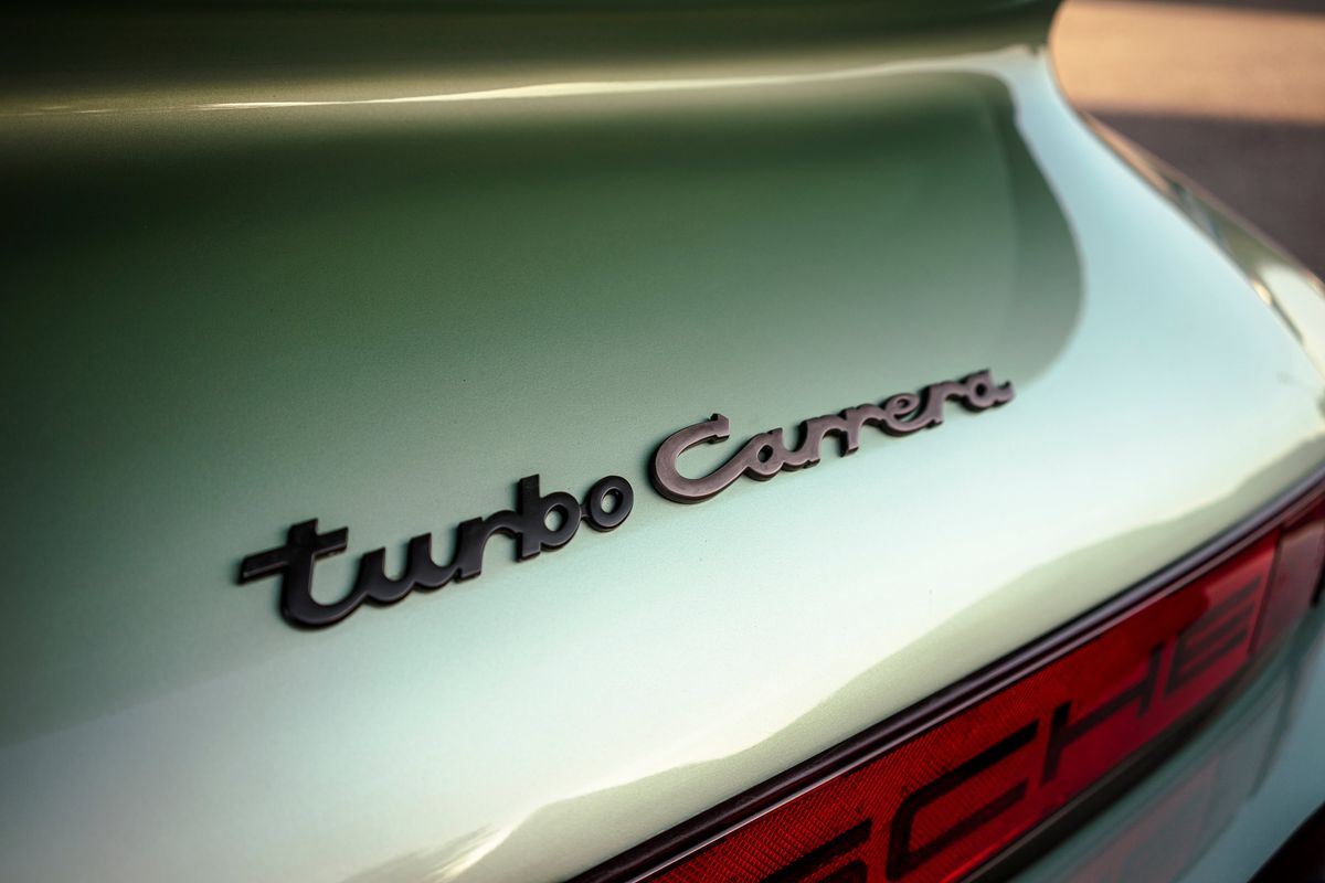 1976 Porsche 930 in Ice Metallic Green. Rear decklid shows "turbo Carrera" badge with dark 'turbo' and bronze 'Carrera' script.