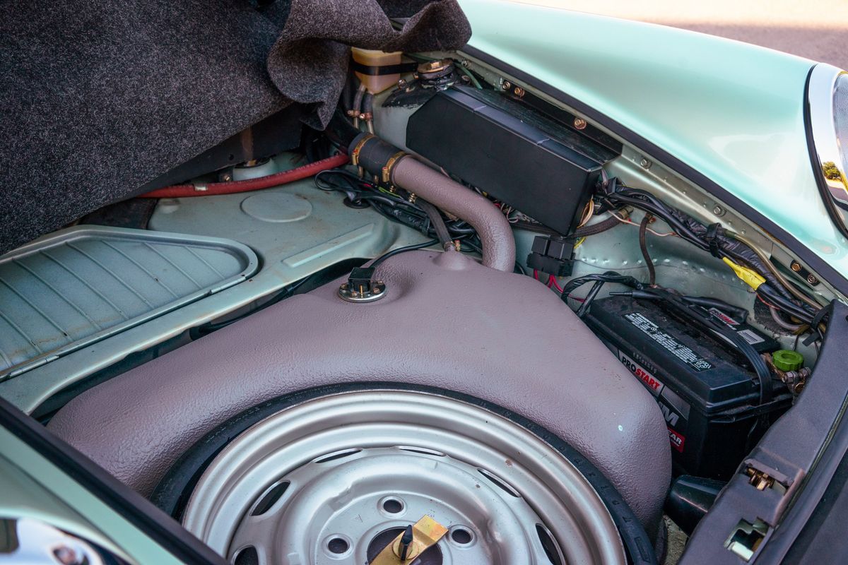 Vintage 1976 Porsche 930 frunk in Ice Metallic Green, showing steel spare wheel, fuel tank, and Prostart battery.