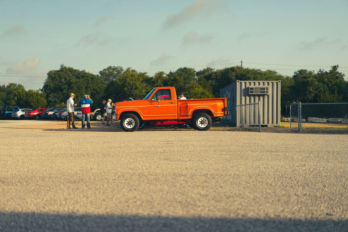 Vibrant orange 1978 Ford F-150 Ranger XLT Dentside pickup at a car meet, featuring white steel rims & chrome trim.