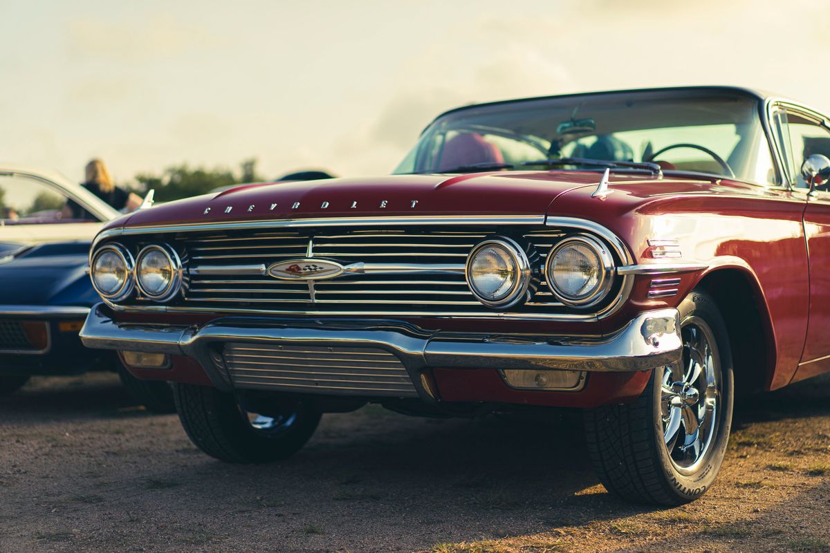 Front view of a shiny red 1960 Chevrolet Impala at a car show, featuring chrome grille, dual headlights, and multi-spoke rims.