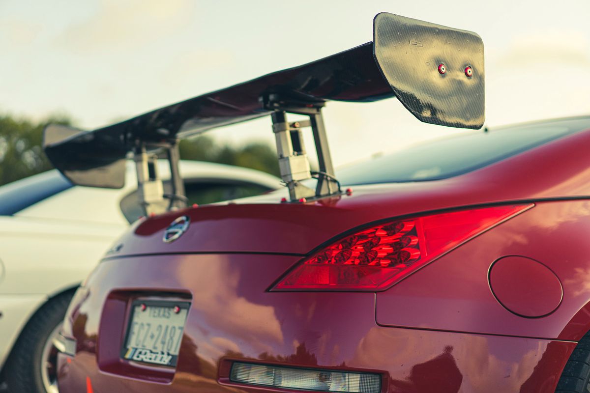 Red Nissan 350Z with prominent carbon fiber GT wing, distinctive LED taillights, and Texas license plate.