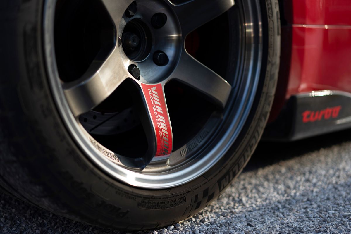 Red sports car's gunmetal Rays Volk Racing 5-spoke rims, Michelin Pilot Sport tires, and red 'turbo' side trim.