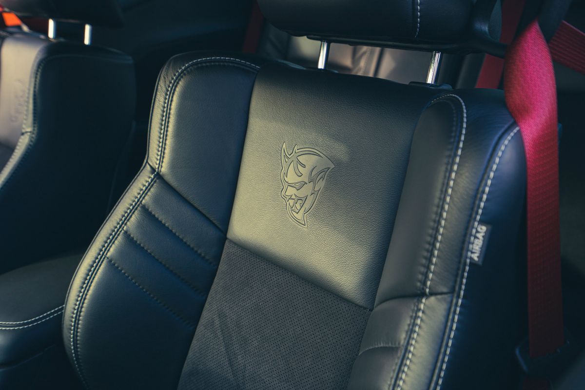 Dodge Challenger SRT Demon black leather interior with embossed Demon logo, white stitching, perforated inserts, and red seatbelt.