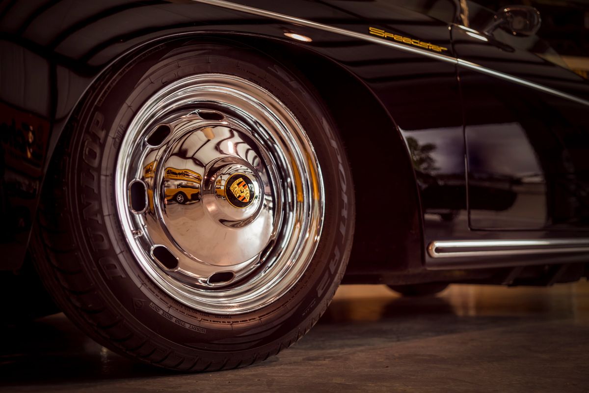 Gloss black Porsche 356 Speedster fender detail, showing gold "Speedster" badging, chrome side trim, and full-disc hubcap with Porsche crest.