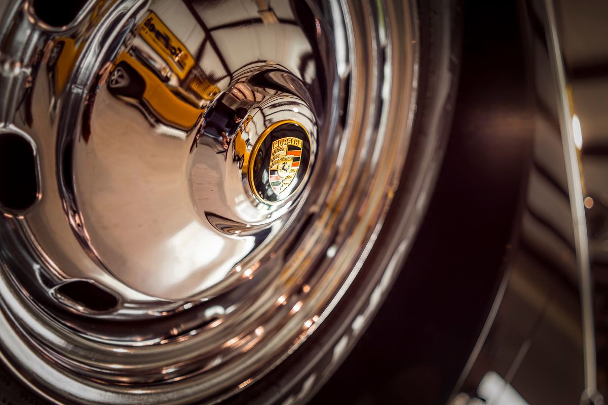 Detail of a classic Porsche's gleaming chrome wheel hubcap with crest, reflecting the vintage yellow paint of the vehicle.